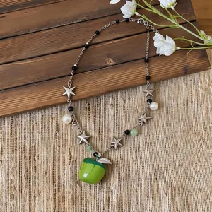Fresh beaded necklace with green apple pendant, silver stars, and white pearls on wooden background.