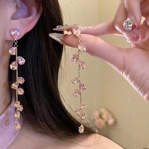 Dettaglio di lunghi orecchini nappa con zirconi a goccia rosa e design a foglia dorata