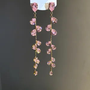 Primo piano di orecchini a nappa dorati con scintillanti zirconi rosa a goccia.