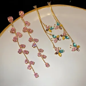 Dettaglio orecchini con nappa in zircone rosa e farfalla colorata su piatto bianco
