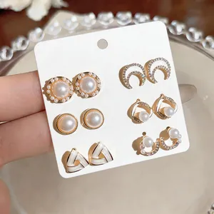 Detailed view of six pairs of elegant pearl and rhinestone stud earrings on white card.