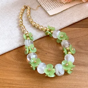 Close-up of acrylic green flower and gold beaded necklace on a wooden surface