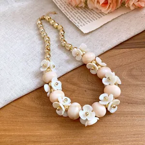 Close-up of acrylic oval bead necklace with white floral accents and gold beads.