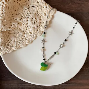 Detail view of a fresh apple pendant necklace with stars and pearls on a white plate.