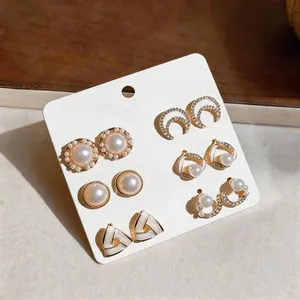 Detailed view of six pairs of elegant pearl and rhinestone stud earrings on white card.