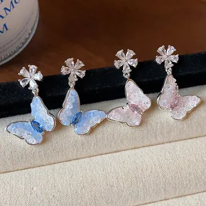 Dettaglio di eleganti orecchini a lobo a farfalla e fiore con zirconi scintillanti