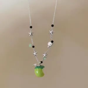 Close-up detail of silver chain necklace featuring a green apple pendant and star charms