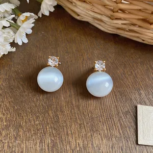 Detailed macro view of minimalist gold stud earrings with white cat eye stone and zircon