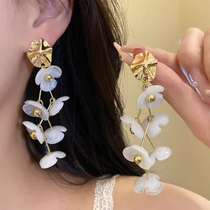 Detailed close-up view of elegant white acrylic flower drop earrings with gold accents.