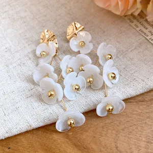 Close-up of elegant white acrylic flower drop earrings with golden beads and marble texture