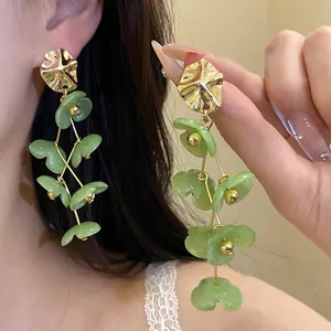 Detail view of long green acrylic flower dangle earrings with gold metal accents