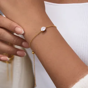 Detail view of 18k gold plated stainless steel bracelet with oval white zircon on wrist.