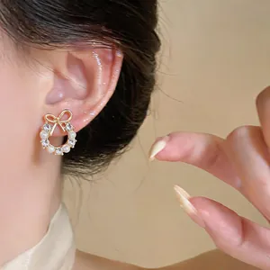 Close-up of elegant gold bow earrings with pearls and rhinestones on a model's ear