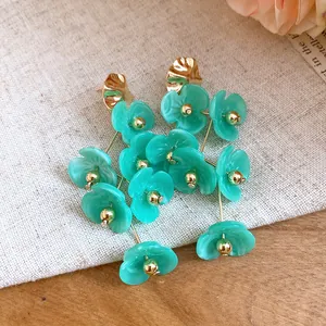 Close-up of elegant teal acrylic flower dangle earrings with gold bead accents and metal studs