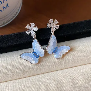 Vista dettagliata di orecchini a lobo farfalla e fiore in zircone con pietre blu.