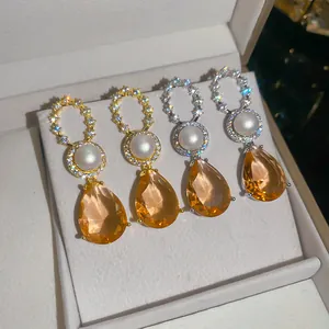 Detailansicht von 18k vergoldeten Ohrhängern mit Perle und champagnerfarbenen Steinen.