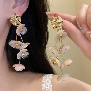 Close-up of elegant long dangle earrings with pink acrylic flower petals and gold accents.