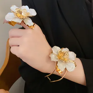 Detailed view of white enamel and gold flower ring and bangle set on black blazer