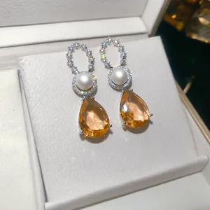 Nahaufnahme von vergoldeten Zirkonia-Perlenohrringen mit funkelnden orangefarbenen Tropfen.