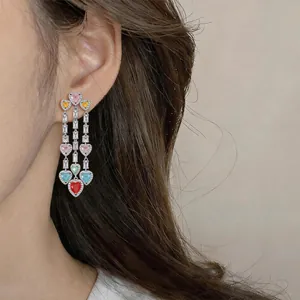 Detail of colorful heart-shaped crystal tassel earrings worn on a model's ear.
