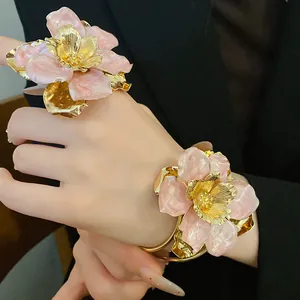 Close-up of pink enamel flower ring and bracelet set with golden finish on model's hand