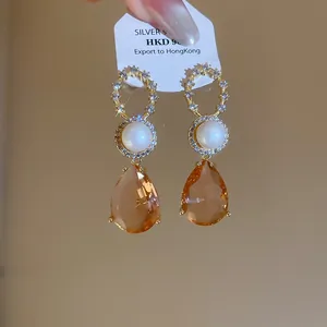 Detailansicht der 18 Karat vergoldeten Tropfenohrringe mit Zirkonia, Perle und Bernstein.