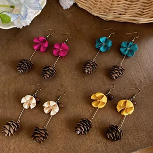 Handmade floral earrings with pinecone charms in various colors on wooden surface.