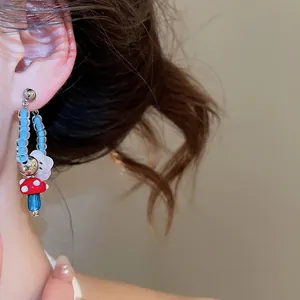 Retro red mushroom and blue glass bead earrings with flower charm on model's ear