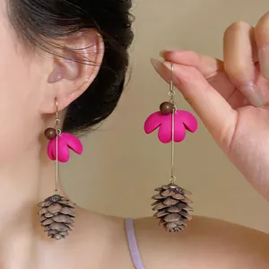 Detail view of pink floral drop earrings with pinecone pendants worn by a model