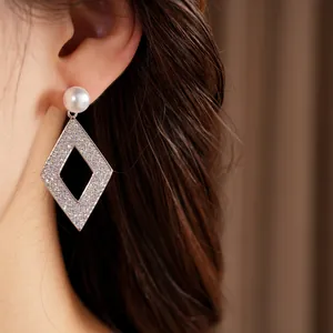 Vue détaillée d'une boucle d'oreille argentée avec perle et pendant losange en zircon.