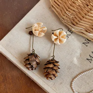 Detail view of flower hook earrings with brown pinecone pendants on linen