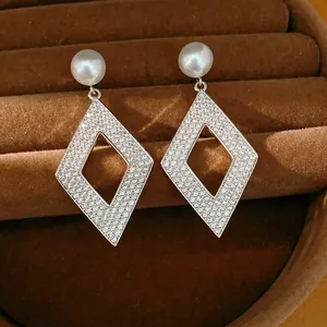 Gros plan de boucles d'oreilles losange élégantes avec zircons et perles blanches.