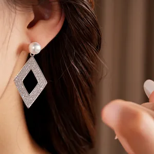 Détail rapproché de boucles d'oreilles pendantes losange évidé en zircon avec perle élégante