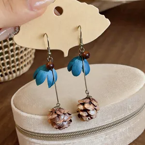 Detailed view of handmade flower drop earrings with blue petals and pinecone accents