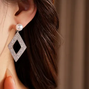 Détail de boucles d'oreilles pendantes losanges ajourés avec zircons et perle.