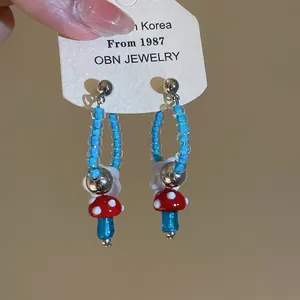 Macro shot of cute retro red mushroom and blue bead dangle earrings with flower detail