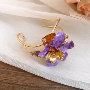 Detailed view of an elegant gold cuff bracelet featuring a large purple enamel flower.