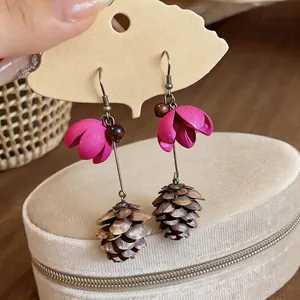 Close-up of floral and pinecone drop earrings with elegant pink flower and natural cone