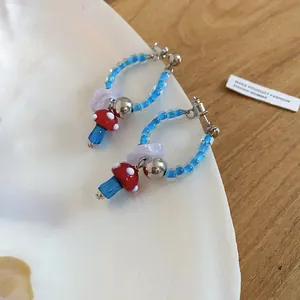 Detailed macro view of red and blue mushroom glass earrings with blue beaded hoops.