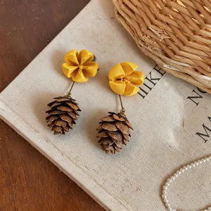 Macro view of yellow fabric flower and brown pinecone earrings with natural textures.