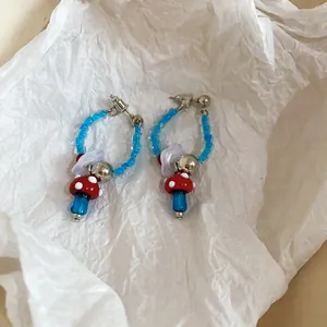 Detail view of handmade glass mushroom earrings with blue beads and white flower charms