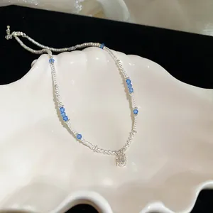 Close-up detail of a pearl and blue crystal beaded necklace with a square pendant on a shell.