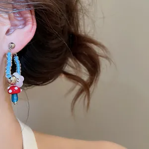 Close-up of a cute handmade beaded earring with red mushroom and blue flower charms.