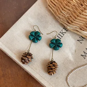Detailed view of teal flower and brown pinecone drop earrings on linen background