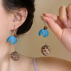 Detailed view of handmade flower and pinecone tassel earrings worn on ear and held.