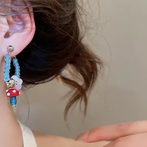 Detailed macro shot of retro red and blue mushroom beaded earring with white flower charm.