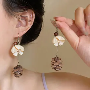 Close-up shot of elegant flower drop earrings featuring a unique pinecone pendant on a model