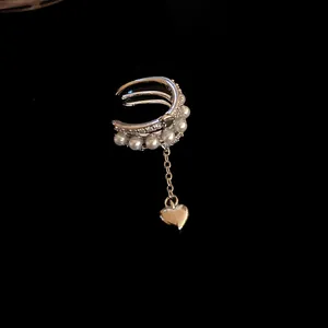 Detail of silver triple-band ear cuff with pearls and heart pendant on black background.