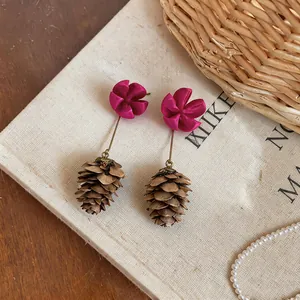 Detail shot of magenta flower and pinecone dangle earrings on a neutral background