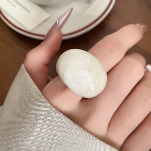 Macro shot of a minimalist cream resin ring with marble swirl on a manicured hand